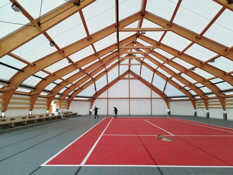 Wnętrze łukowej hali sportowej z drewnianą konstrukcją łukową i membranowym dachem