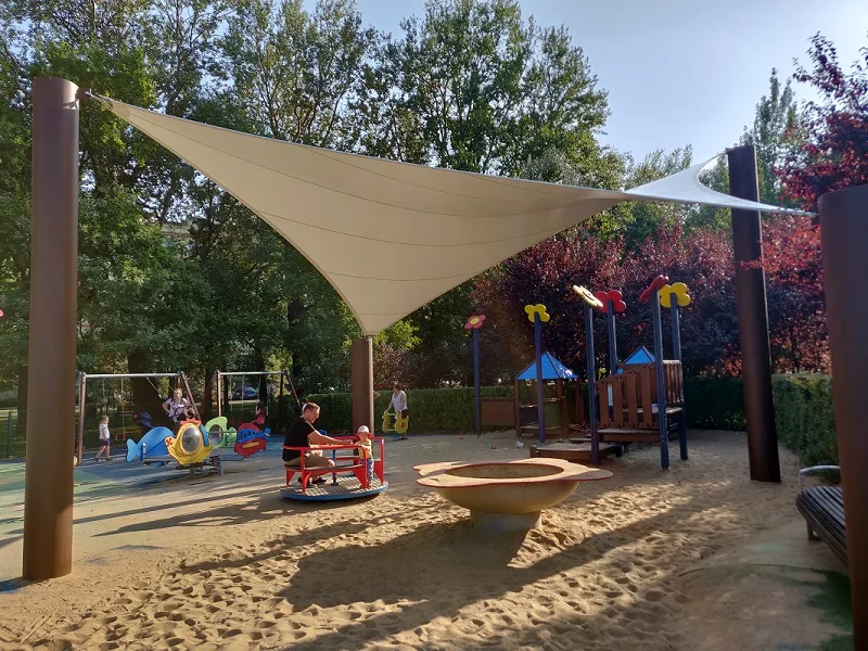 Żagiel membranowy nad placem zabaw z kolorowymi urządzeniami