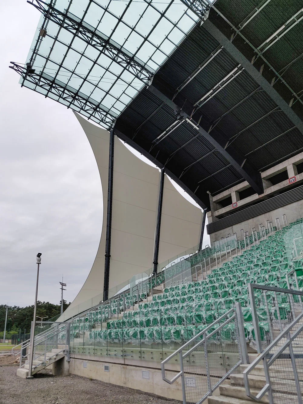 Membranowe zadaszenie trybuny stadionu nad rzędami zielonych siedzeń
