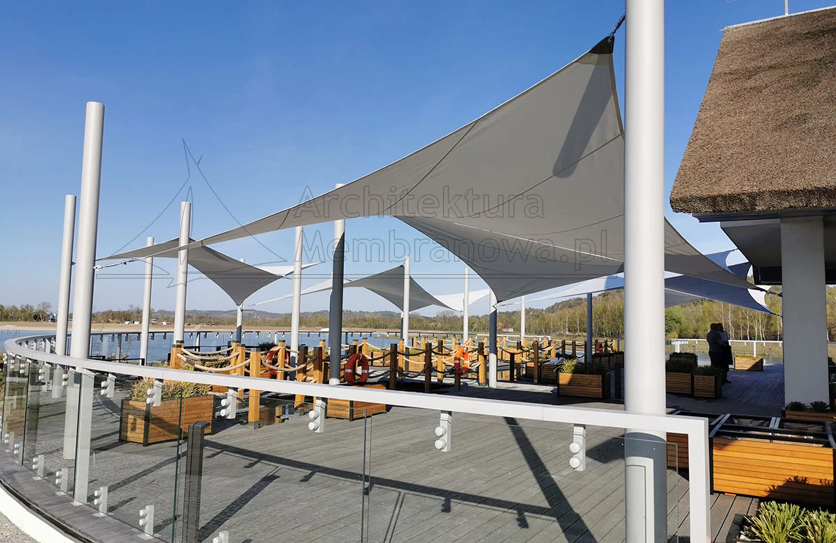Membranowe zacienienie tarasu restauracji nad jeziorem szeregiem żagli na masztach