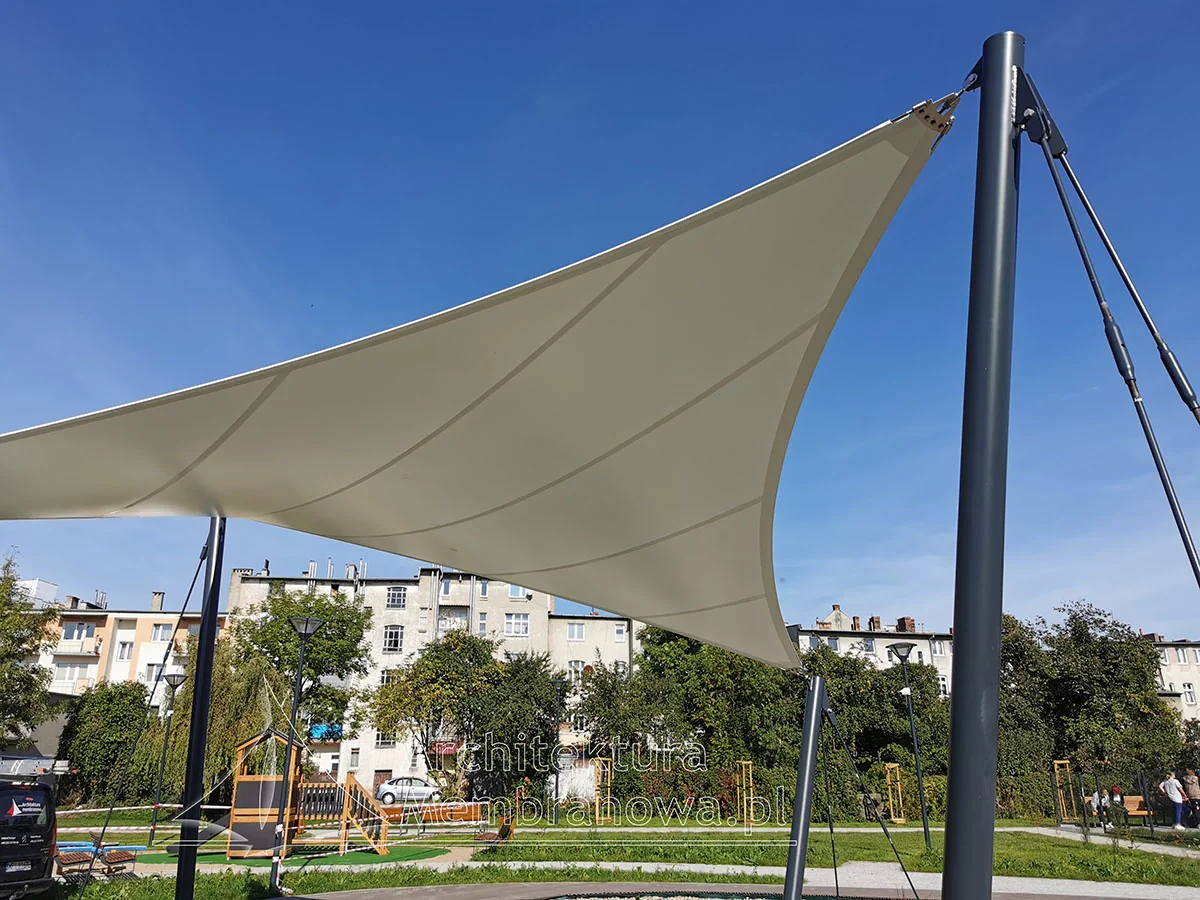 Efektowny napinany żagiel membranowy nad placem zabaw na masztach, na tle błękitnego nieba